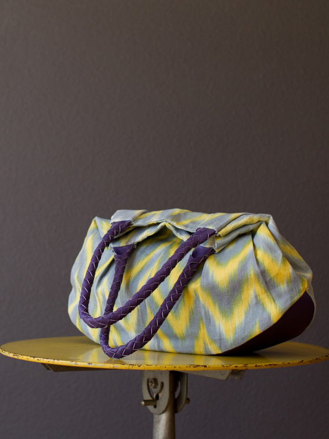 Gefaltete handgemachte Schultertasche von KikieKoch Procida aus gelb-grau gezickzacktem Ikat Stoff. Boden und Träger aus violettem Rindsleder.