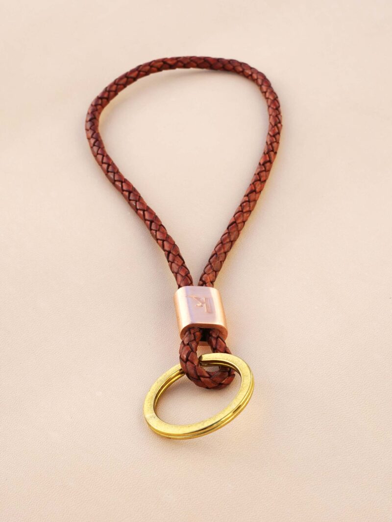 Handgemachter Schlüsselbändel von KikieKoch Procida, rund geflochten aus rostrotem Rindsleder, mit geprägter Kupferklemme und grossem Schlüsselring aus Messing.