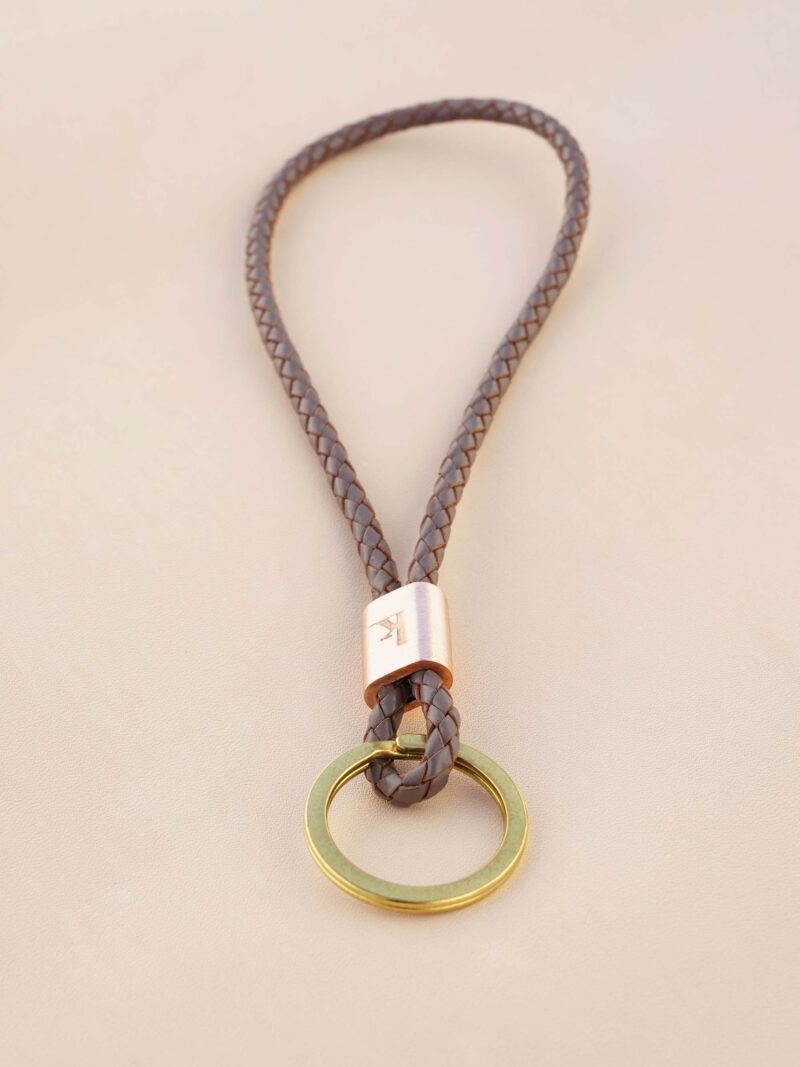Handgemachter Schlüsselbändel von KikieKoch Procida, rund geflochten aus braungrauem Rindsleder, mit geprägter Kupferklemme und grossem Schlüsselring aus Messing.