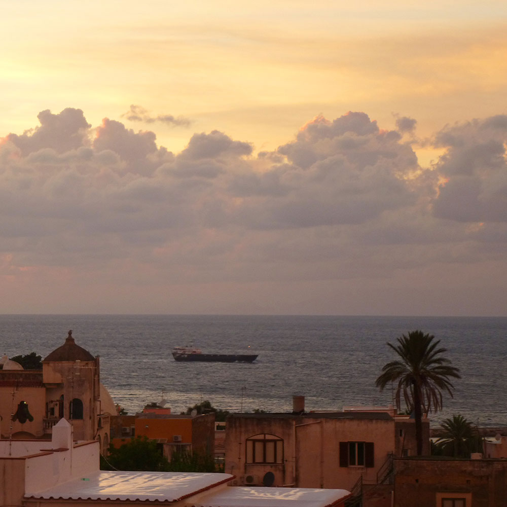 Mediterranes Inselstädtchen Procida mit Palme und kleinem Frachter in der Abendsonne